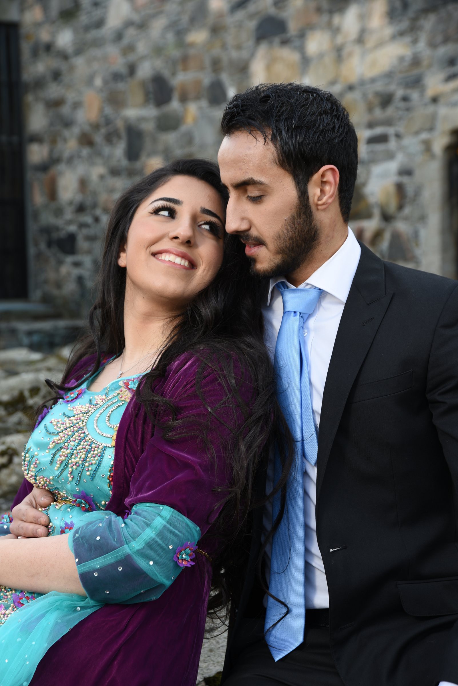 Par fotografert tett sammen foran en steinvegg