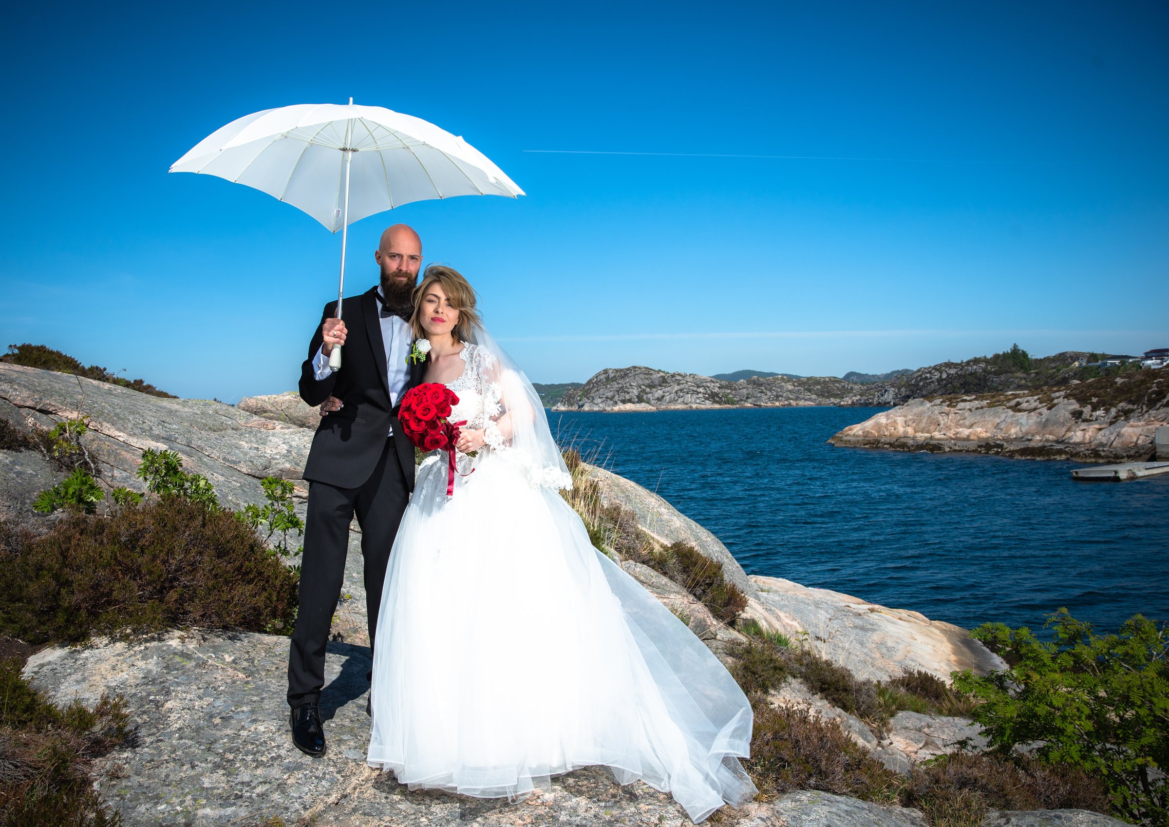 Brudepar ved kysten under en hvit paraply